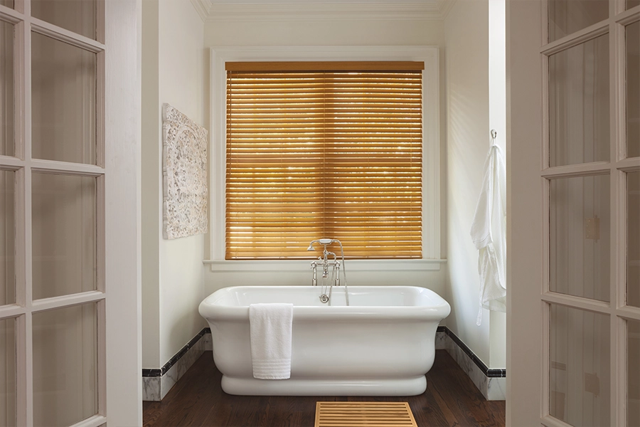 Premium faux wood blinds offer similar benefits to interior shutters but with a lower price tag. Brown faux wood blinds on a window over a bathtub