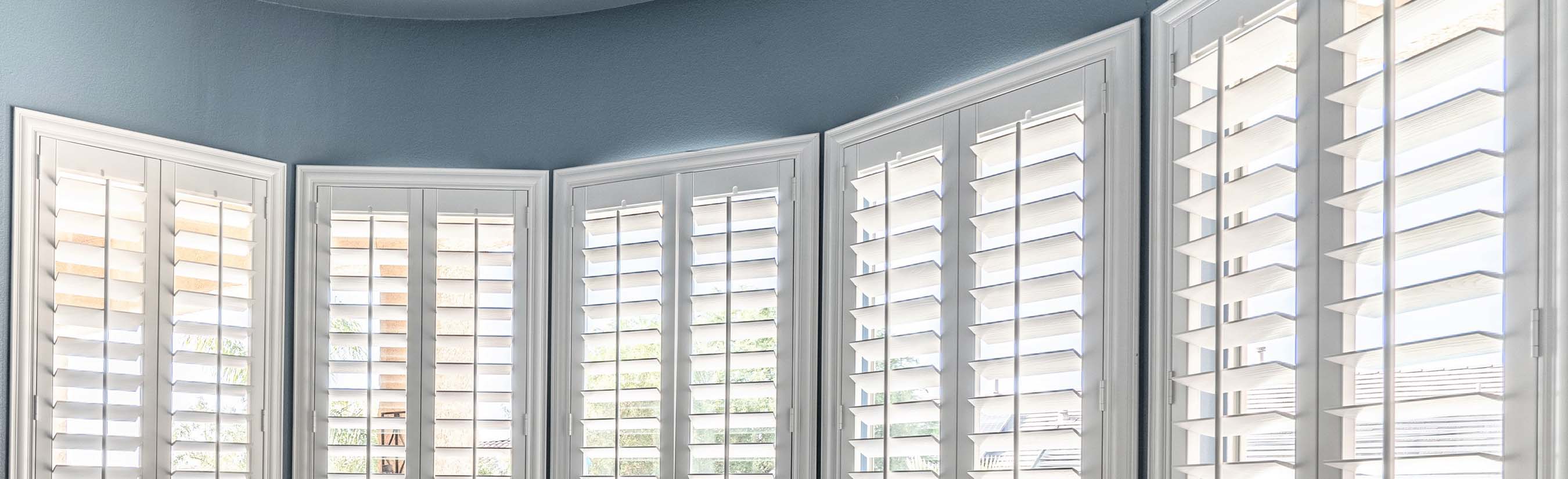 White eyebrow shutters in a bay window style within a living room.