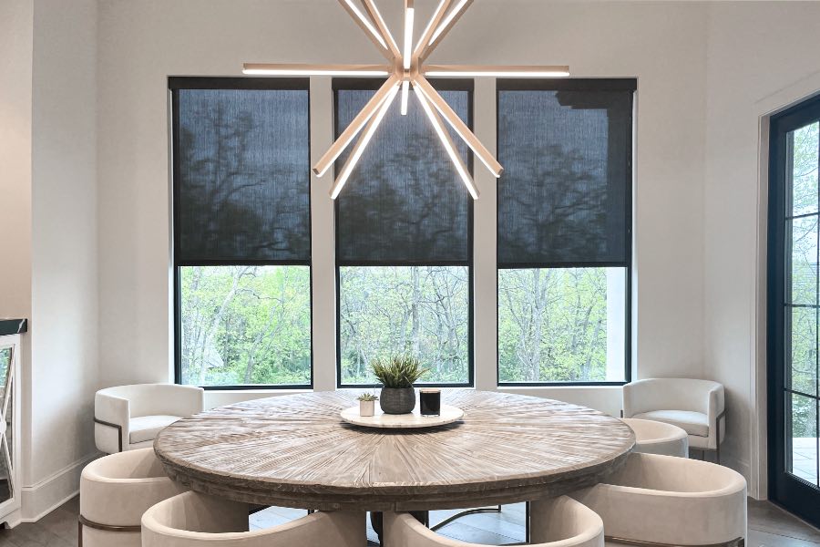 Put motorized shades on tall or high up windows so you don't have to reach far to use them. Black motorized shades on three windows in a beige dining room