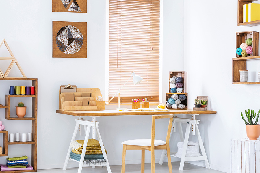 Light oak wood blinds add a natural element to your living space.  Wood blinds in a white and airy craft corner.